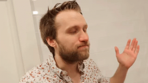 A Man With A Beard Is Looking At Himself In A Bathroom Mirror . GIF