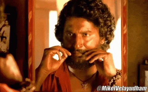 A Man With A Beard Is Looking At Himself In A Mirror With @Mikelvelayudham Written On The Bottom GIF