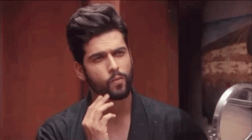 A Man With A Beard Is Looking At Himself In The Mirror GIF