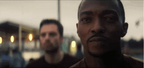 A Man With A Beard Is Looking At The Camera While Another Man Looks On . GIF