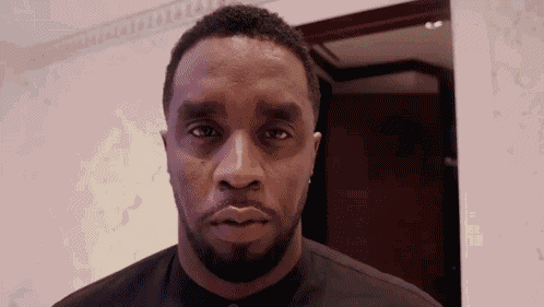 A Man With A Beard Is Looking At The Camera While Wearing A Black Shirt . GIF