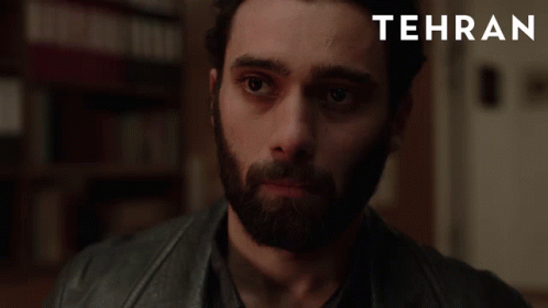 A Man With A Beard Is Looking At The Camera With Tehran Written In The Corner GIF