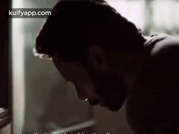 A Man With A Beard Is Looking Down At Something . GIF