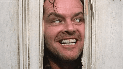 a man with a beard is looking through a door and smiling .
