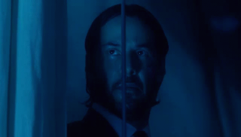a man with a beard is looking through a window with a blue light behind him