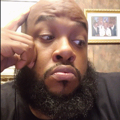 A Man With A Beard Is Making A Funny Face In Front Of A Framed Picture GIF