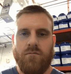 A Man With A Beard Is Making A Funny Face In Front Of A Shelf Of Chemicals . GIF