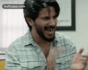 A Man With A Beard Is Making A Funny Face While Clapping His Hands . GIF