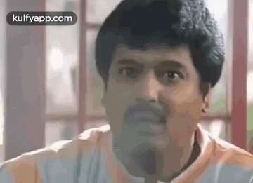 A Man With A Beard Is Making A Funny Face While Sitting In Front Of A Window . GIF