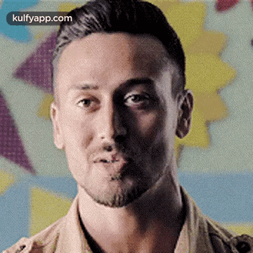 A Man With A Beard Is Making A Funny Face While Standing In Front Of A Colorful Background . GIF