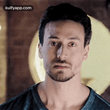 A Man With A Beard Is Making A Funny Face While Wearing A Black Shirt . GIF
