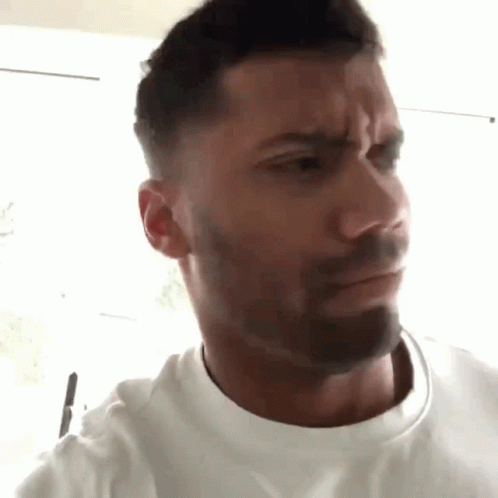 A Man With A Beard Is Making A Funny Face While Wearing A White T-Shirt . GIF