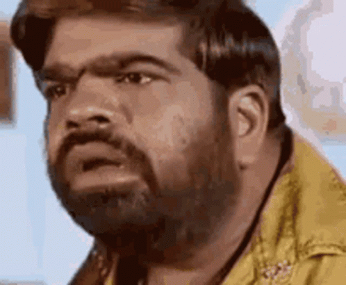 A Man With A Beard Is Making A Funny Face While Wearing A Yellow Shirt . GIF