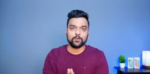 A Man With A Beard Is Making A Funny Face With His Hands Outstretched In Front Of A Blue Wall . GIF