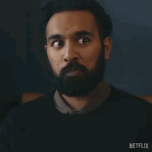 A Man With A Beard Is Making A Surprised Face In A Dark Room . GIF