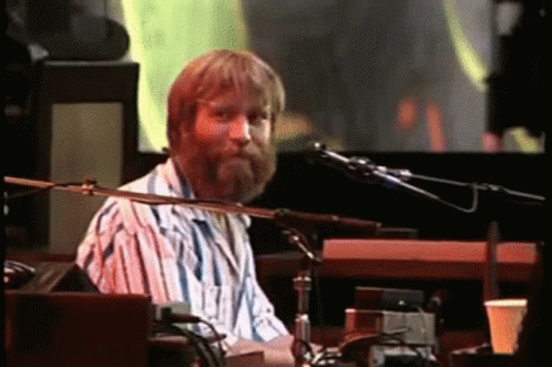 A Man With A Beard Is Playing A Keyboard And Singing Into A Microphone On A Stage . GIF