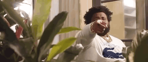 A Man With A Beard Is Pointing At The Camera While Standing In Front Of A Window . GIF