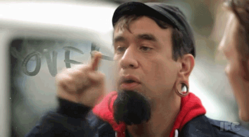 A Man With A Beard Is Pointing At The Word Over Written On A Window GIF