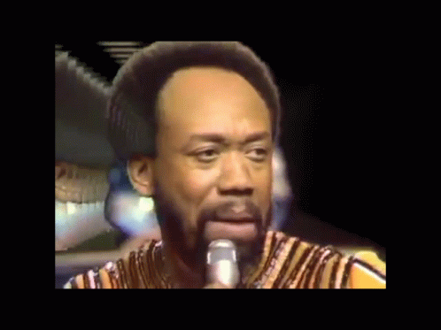 a man with a beard is singing into a microphone while wearing a striped shirt