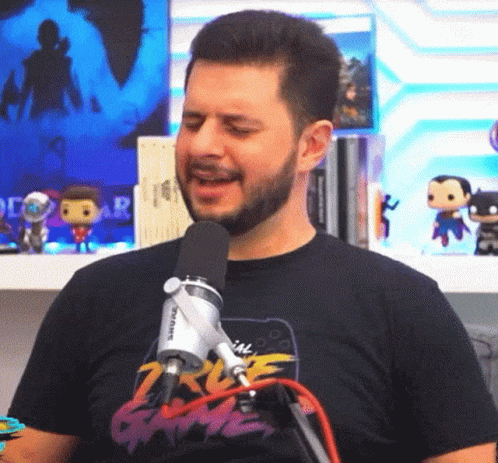 A Man With A Beard Is Singing Into A Microphone While Wearing A T-Shirt That Says 2K Game GIF
