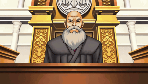 A Man With A Beard Is Sitting At A Podium In Front Of A Justice Symbol GIF