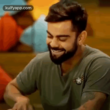 A Man With A Beard Is Sitting At A Table And Smiling . GIF
