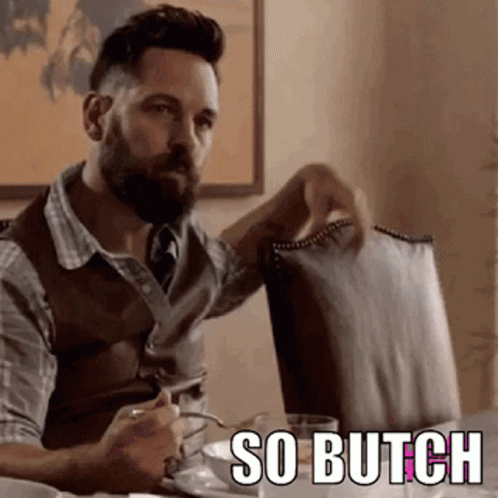 A Man With A Beard Is Sitting At A Table Holding A Chair And A Cup Of Coffee . GIF
