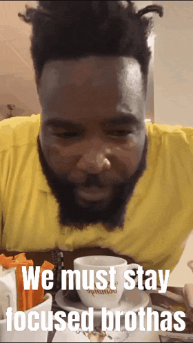 A Man With A Beard Is Sitting At A Table With A Cup Of Coffee And The Words We Must Stay Focused Brothas GIF