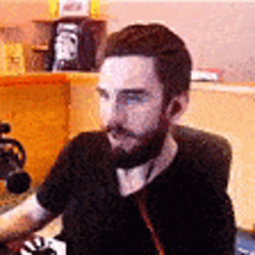 A Man With A Beard Is Sitting At A Table With A Microphone In Front Of Him . GIF