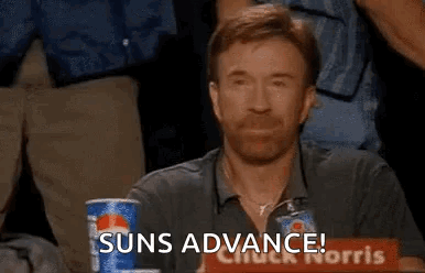 A Man With A Beard Is Sitting At A Table With A Pepsi Can And A Sign That Says Suns Advance . GIF