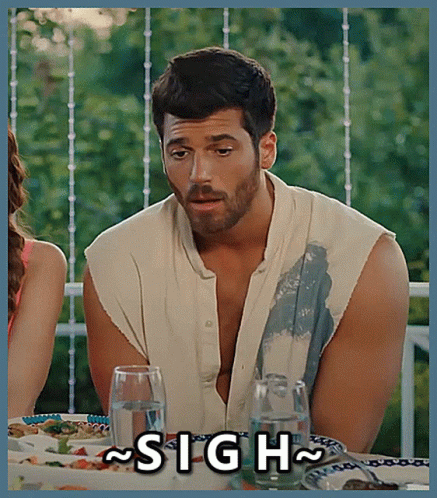 A Man With A Beard Is Sitting At A Table With A Sign That Says Sigh GIF