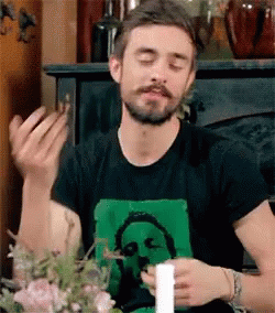 A Man With A Beard Is Sitting At A Table With His Eyes Closed And A Candle In His Hand . GIF