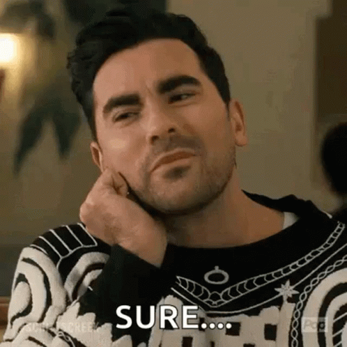 A Man With A Beard Is Sitting At A Table With His Hand On His Chin And Making A Funny Face . GIF