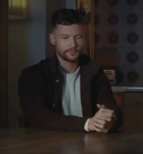 A Man With A Beard Is Sitting At A Table With His Hands Folded In Prayer . GIF