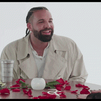 A Man With A Beard Is Sitting At A Table With Red Roses And A Glass Of Water GIF