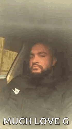 A Man With A Beard Is Sitting In A Car With The Words `` Much Love G '' Written On The Screen . GIF
