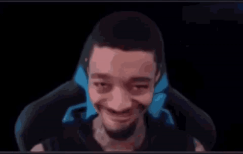 A Man With A Beard Is Sitting In A Chair And Smiling At The Camera . GIF
