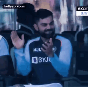 A Man With A Beard Is Sitting In A Chair And Waving His Hands In The Air . GIF
