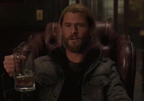 a man with a beard is sitting in a chair holding a beer mug .