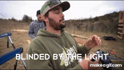 A Man With A Beard Is Sitting In A Chair In A Field With The Words Blinded By The Light Written Above Him . GIF