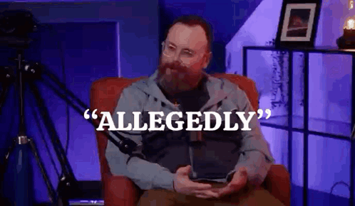 A Man With A Beard Is Sitting In A Chair In Front Of A Microphone Holding A Tablet . GIF