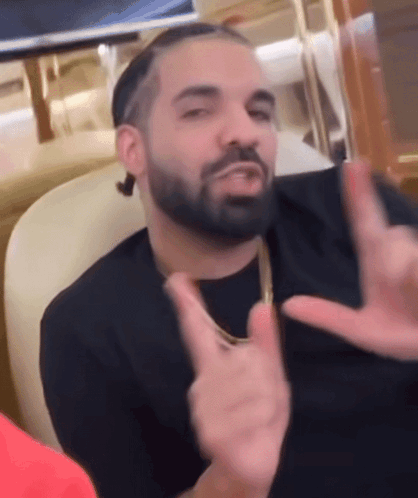 A Man With A Beard Is Sitting In A Chair Making A Peace Sign With His Hands GIF