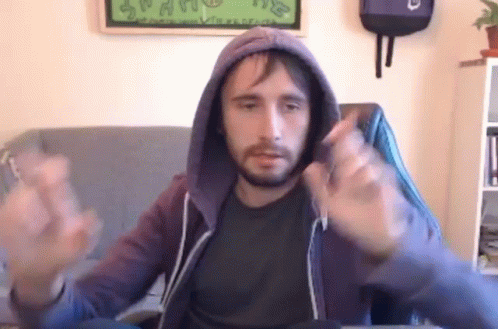 A Man With A Beard Is Sitting In A Chair Wearing A Hoodie And Making A Funny Face . GIF