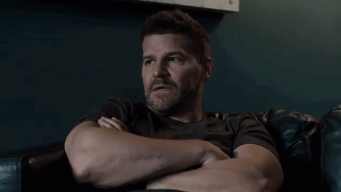 A Man With A Beard Is Sitting In A Chair With His Arms Crossed GIF