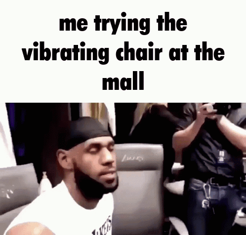 A Man With A Beard Is Sitting In A Chair With The Words Me Trying The Vibrating Chair At The Mall Above Him GIF