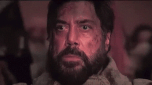 A Man With A Beard Is Sitting In A Dark Room And Looking Up At The Sky . GIF