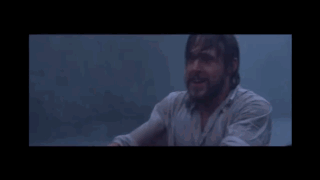 A Man With A Beard Is Sitting In A Dark Room Looking At Something GIF