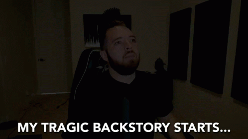 A Man With A Beard Is Sitting In A Dark Room With The Words My Tragic Backstory Starts Behind Him GIF
