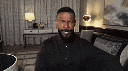 A Man With A Beard Is Sitting In A Living Room GIF