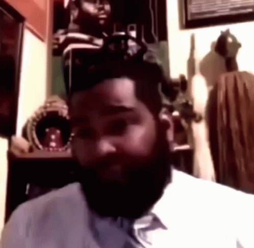 A Man With A Beard Is Sitting In A Room Looking At The Camera GIF